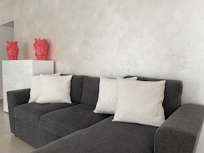 A grey sofa with white patterned cushions, a white side table with red sculptures, and a textured wall. - Arricriati Near Ortigia by Wonderful Italy (Syracuse)