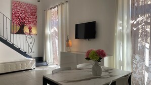 A dining area with a marble table, white chairs, a vase with flowers, a sofa, a staircase, and a TV mounted on the wall. - Arricriati Near Ortigia by Wonderful Italy (Syracuse)