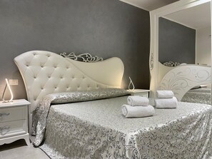 A bedroom with a tufted headboard, a bedside table with a lamp, and a bed with rolled towels. - Arricriati Near Ortigia by Wonderful Italy (Syracuse)