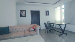 Una sala de estar con sofá, una mesa de centro, una mesa de comedor y sillas, y una puerta.