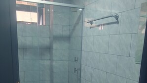 Un baño con ducha de vidrio, dos lavamanos y un inodoro.