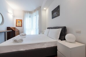 A hotel room with a bed, a bedside table, a lamp, a painting, and a window with curtains. - Italianway Comfort - Gherardini 2 (Milano)