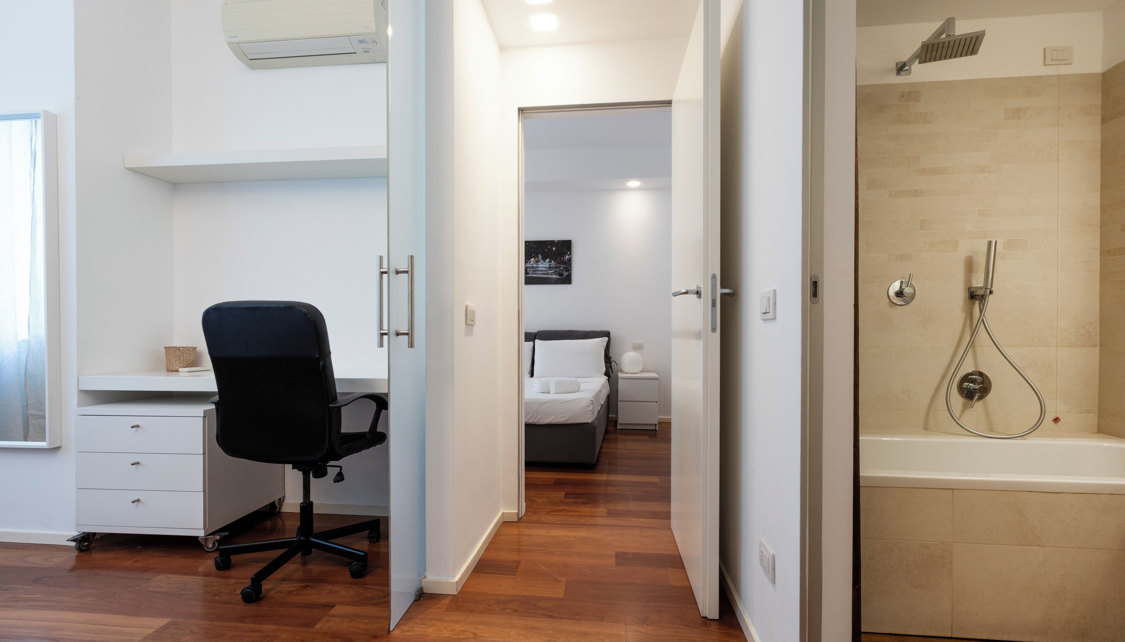 A hotel room with a desk, chair, bed, and a shower area.