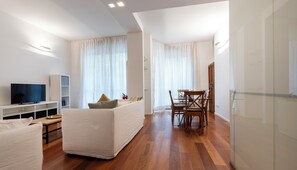 A modern living room with a flat-screen TV, a sofa, a dining table with chairs, and a bookshelf. - Italianway Comfort - Gherardini 2 (Milano)