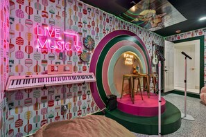 Ein Raum mit einem Neonlichtschild mit der Aufschrift 'LIVE MUSIC', einem Keyboard, Barhocker und einem Mikrofonständer.
