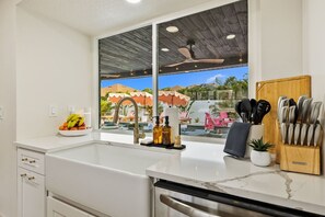 A kitchen with a large window, a fruit bowl, a soap dispenser, and a knife block.