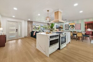 A modern kitchen with white cabinetry, a central island, and a dining area with a table and chairs. - Luxury Resort | Pool•Pickleball•Arcade•Karaoke (Seminole)