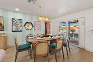 A dining area with a round table set for four, surrounded by wicker chairs with green cushions. - Luxury Resort | Pool•Pickleball•Arcade•Karaoke (Seminole)