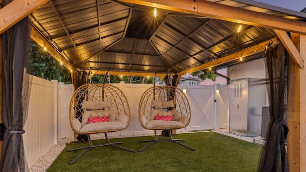 A covered outdoor area with two hanging chairs, artificial grass, and string lights.