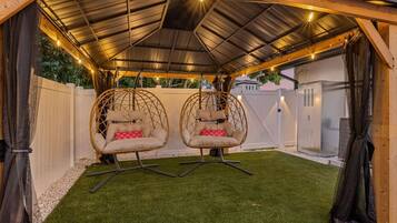 A covered outdoor area with two hanging chairs, artificial grass, and string lights.
