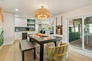A modern kitchen with white cabinets, a dining table set for four, and a large window overlooking a green outdoor area.