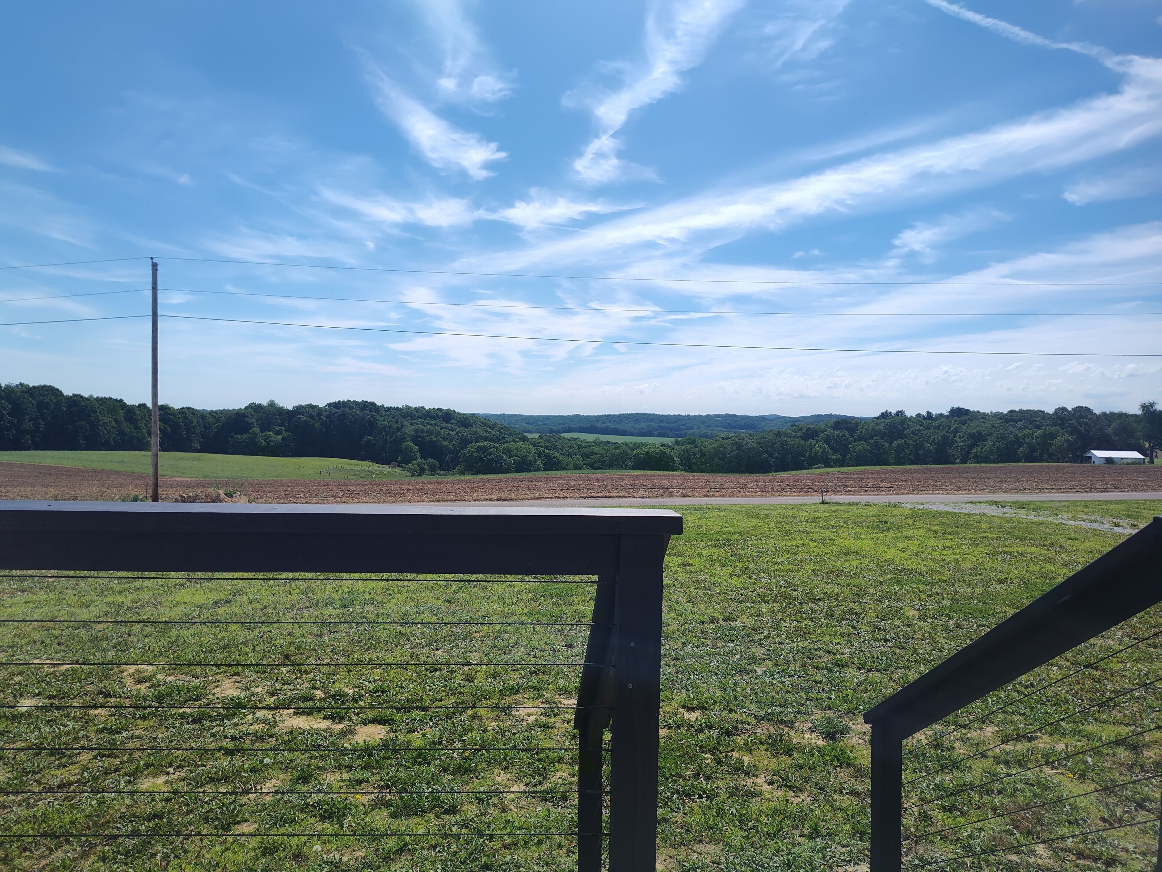 A rural landscape with a fence, a road, and a distant white building.