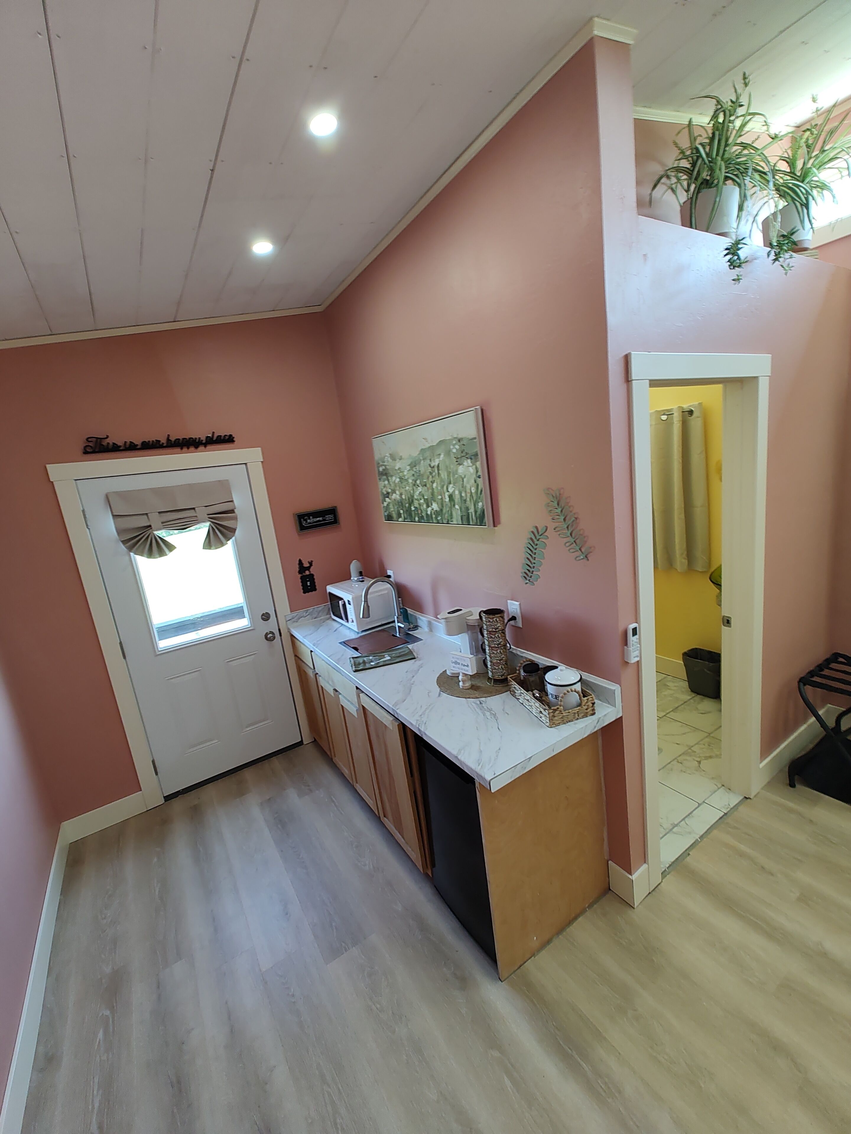A kitchen with a white countertop, a microwave, and a coffee maker. There is a door with a window and a sign above it.