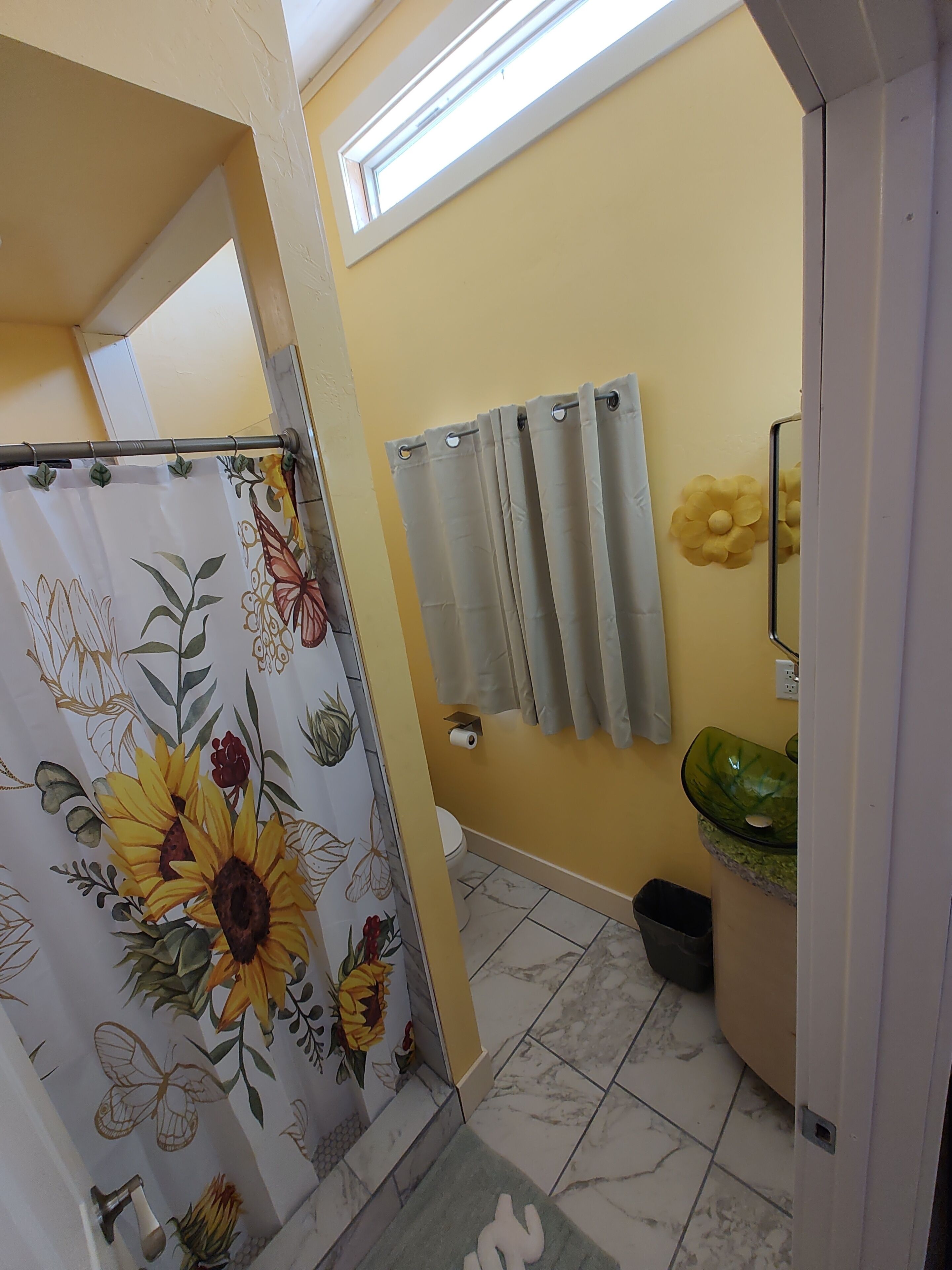 A bathroom with a toilet, a sink with a green basin, a shower curtain with floral patterns, and a towel rack with two towels.