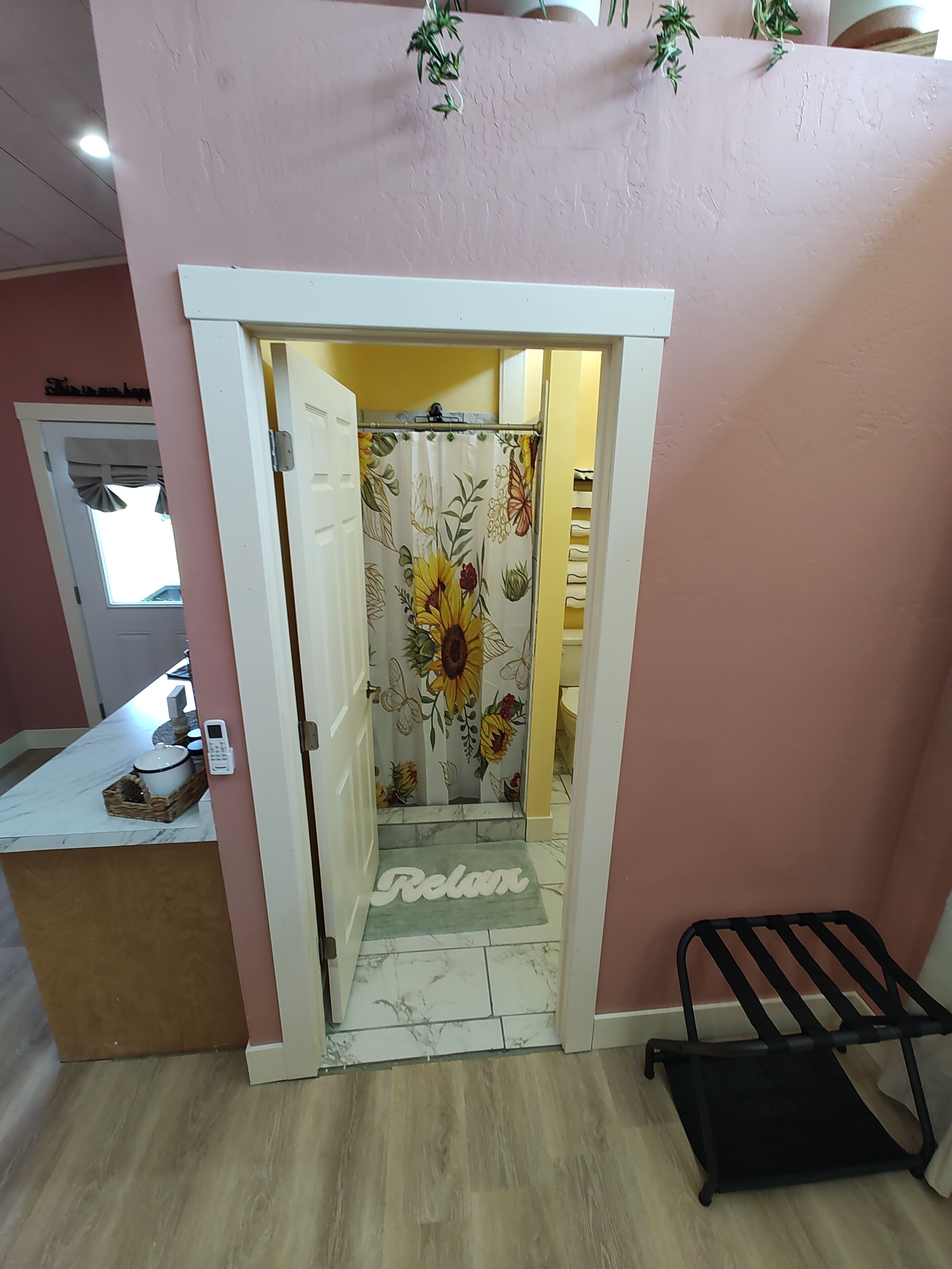 A bathroom with a floral shower curtain, a 'Relax' mat, a black towel rack, and a marble countertop with a basket.
