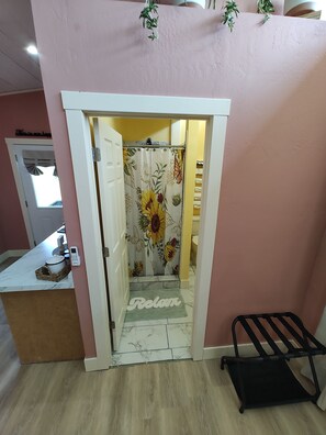 A bathroom with a floral shower curtain, a 'Relax' mat, a black towel rack, and a marble countertop with a basket.