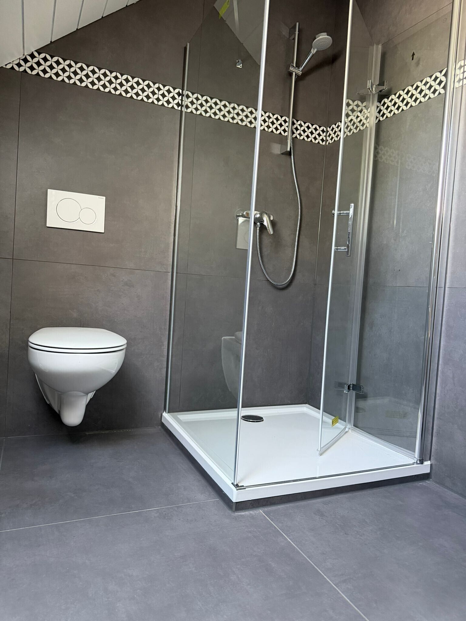 Ein modernes Badezimmer mit einer gläsernen Duschkabine, einer weißen Toilette und einer gemusterten Fliesenleiste.