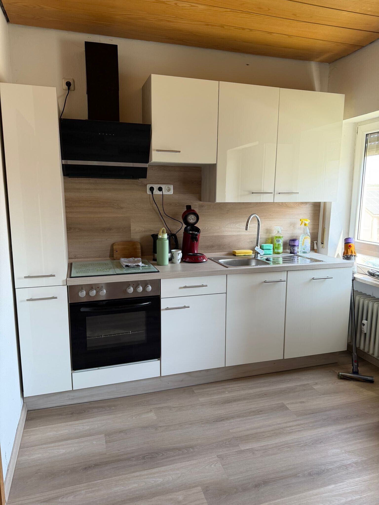 Una cucina moderna con pensili bianchi, una cappa aspirante nera, forno integrato, macchina per caffè e una finestra che offre luce naturale.