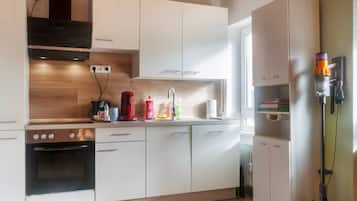 Una cucina moderna con mobili bianchi, forno integrato, macchina da caffè e aspirapolvere.