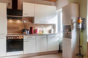 Una cocina moderna con armarios blancos, horno empotrado, cafetera y aspiradora.