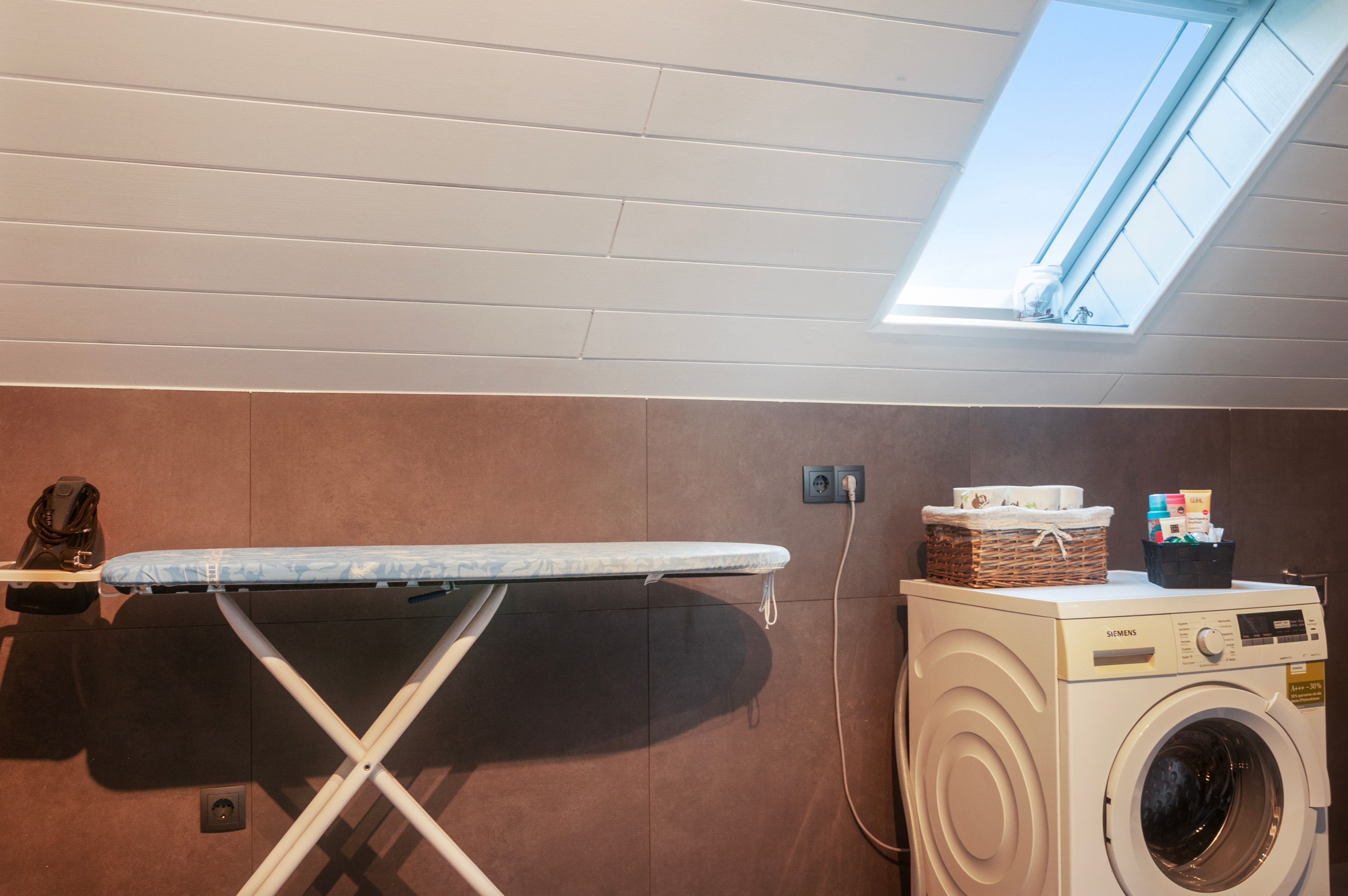 A laundry room with a washing machine, an ironing board, and a skylight.