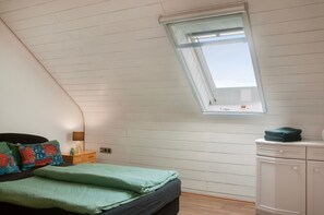 A bedroom with a sloped ceiling, a skylight, a bed with green bedding, a nightstand with a lamp, and a dresser. - Apartment 'Ferienwohnung Markt Bibart' (Markt Bibart)