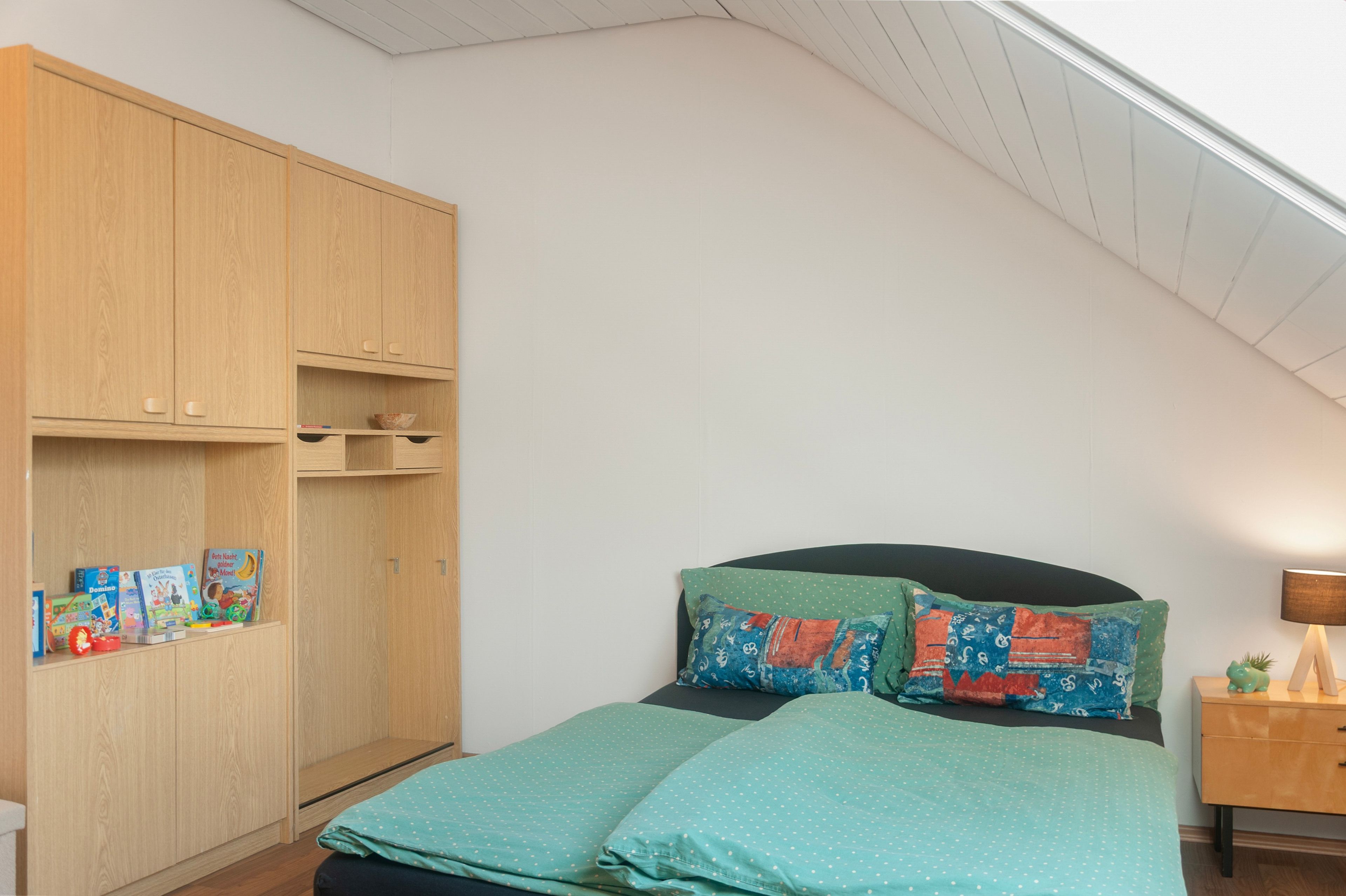 Un dormitorio con un armario de madera, una cama con ropa de cama de lunares y una mesita de noche con una lámpara.