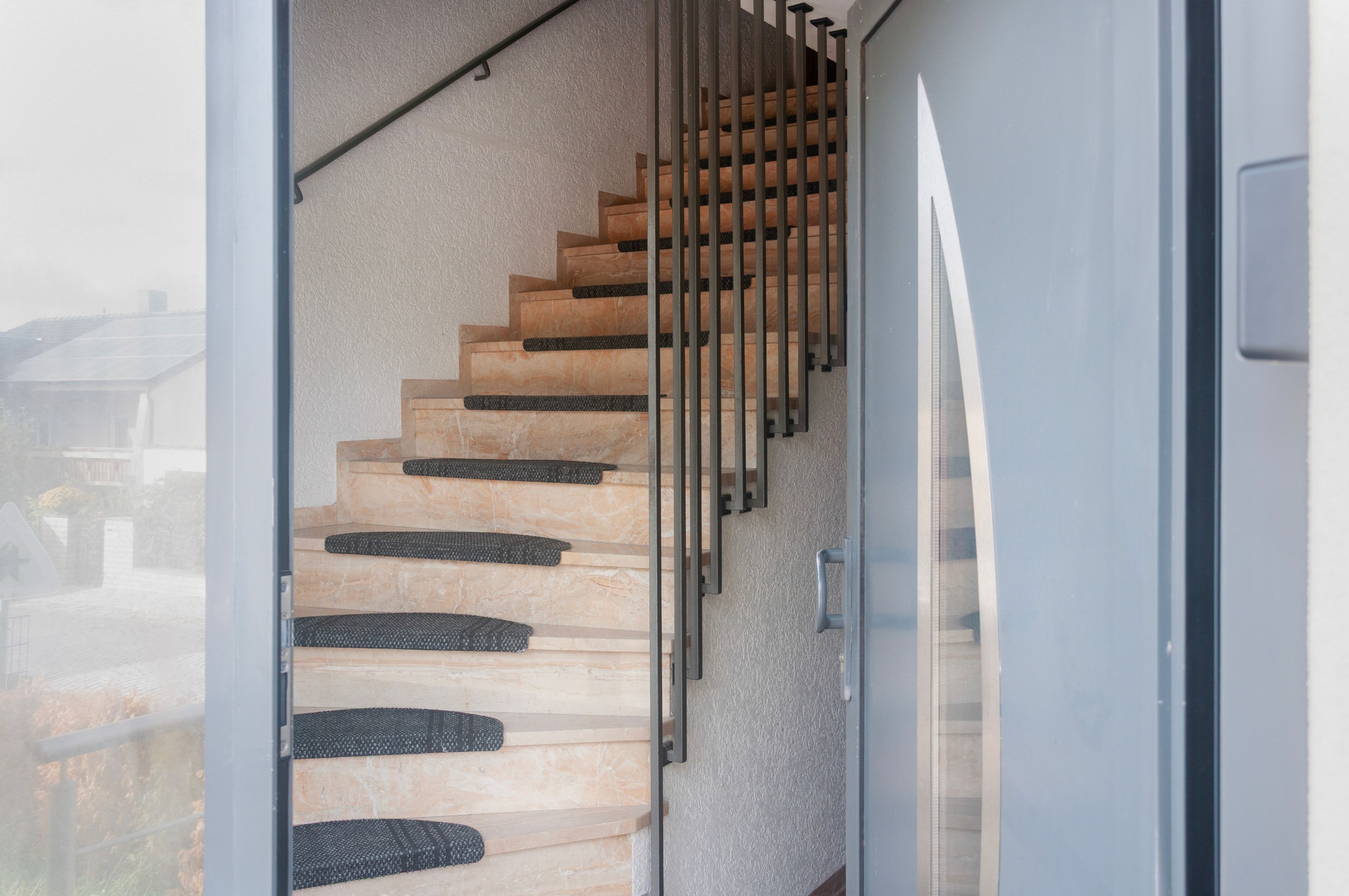 A staircase with wooden steps and black rubber treads, leading to a glass door.