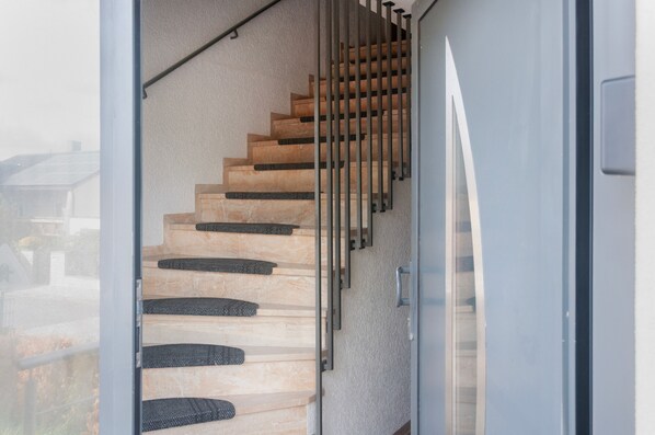 Una escalera con peldaños de madera y bandas antideslizantes negras, que conduce a una puerta de cristal.