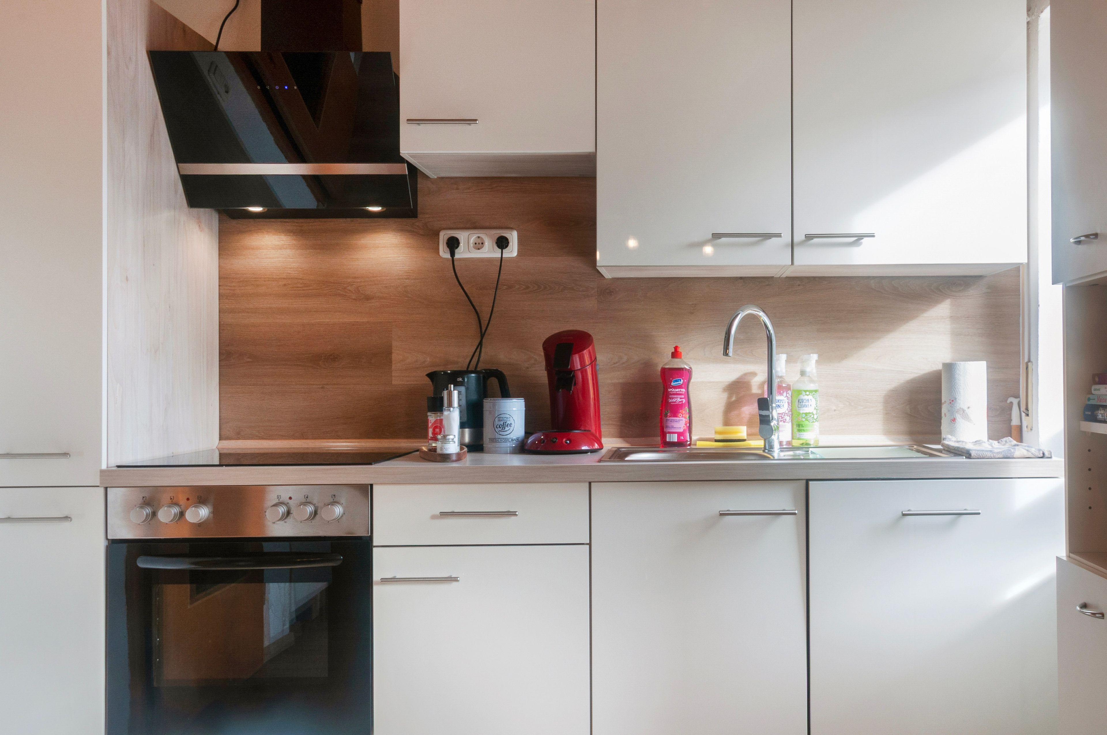 A modern kitchen with white cabinets, a stainless steel oven, a coffee machine, and a kettle.