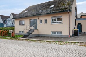 A two-story building with a tiled roof, a staircase leading to the entrance, and a paved driveway. - Apartment 'Ferienwohnung Markt Bibart' (Markt Bibart)