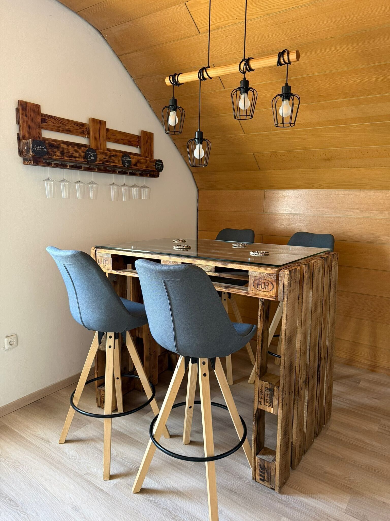 Comedor con mesa de madera, dos taburetes de bar y una lámpara colgante.