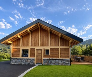 A wooden cabin with a stone foundation, a sloped roof, and a deck with outdoor furniture. - At Ginou - Jogidi Chalet (Saint-Sorlin-d'Arves)