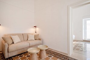 A minimalist living room with a sofa, two side tables, a patterned rug, and a wall-mounted lamp. - ALL Chiantera – Elegant Puglian Retreat with Rooftop Sea Views (Polignano a Mare)