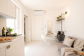 A compact kitchen with white cabinets, a dining area with white chairs, a sofa, and a small table with wine glasses. - ALL Chiantera – Elegant Puglian Retreat with Rooftop Sea Views (Polignano a Mare)