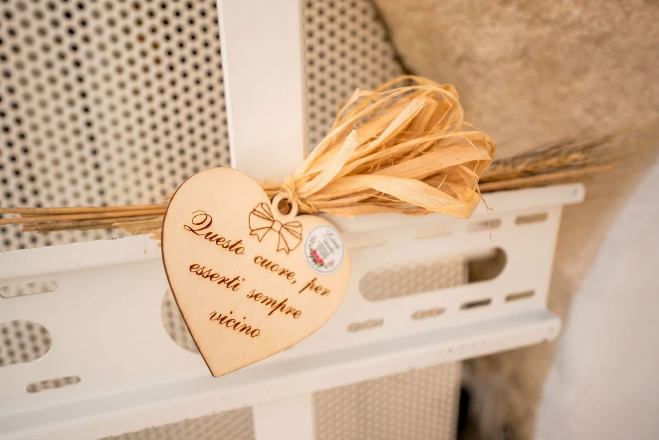 Une plaque en bois en forme de cœur, portant une inscription, attachée à un ruban noué en forme de nœud, posée sur une étagère blanche.