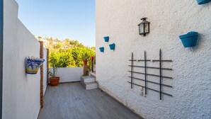 A narrow outdoor corridor with a white textured wall, a potted plant, and a metal rack. - Cubo's Casa Mediterranea BBQ & Terrace / near beach / free wifi (Málaga)