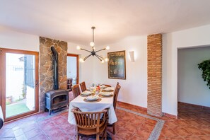 Un comedor con chimenea de piedra, una mesa lista para cuatro personas y una lámpara colgante.
