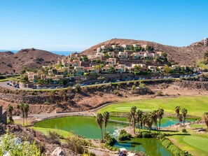 Um resort numa encosta com edifícios modernos, um campo de golfe e um corpo de água.