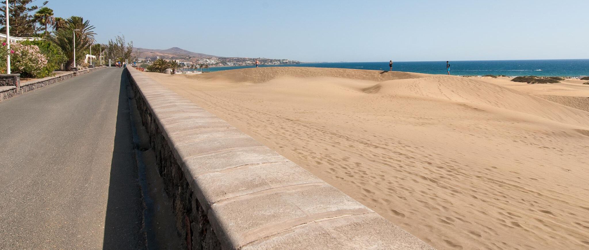 Eine Küstenstraße mit einer Sanddüne rechts und einer asphaltierten Straße links.