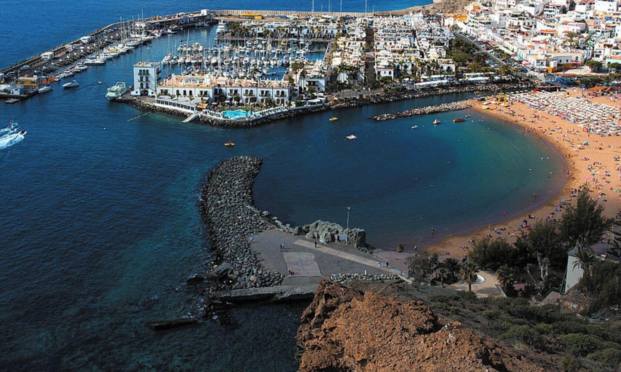 Un pueblo costero con un puerto deportivo, playa y costa rocosa.