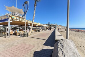 A beachfront restaurant with outdoor seating and palm trees. - Meloneras Bahia H33 by VillaGranCanaria (Maspalomas)