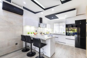 A modern kitchen with a central island, bar stools, and a refrigerator. - Meloneras Bahia H33 by VillaGranCanaria (Maspalomas)