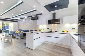 A modern kitchen with a central island, built-in appliances, and a dining area with a sofa and coffee table. - Meloneras Bahia H33 by VillaGranCanaria (Maspalomas)