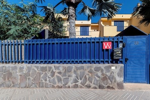 Ein blaues Metalltor, eine Steinmauer, eine blaue Tür mit einer Nummer und ein rotes Schild mit einem weißen Buchstaben.