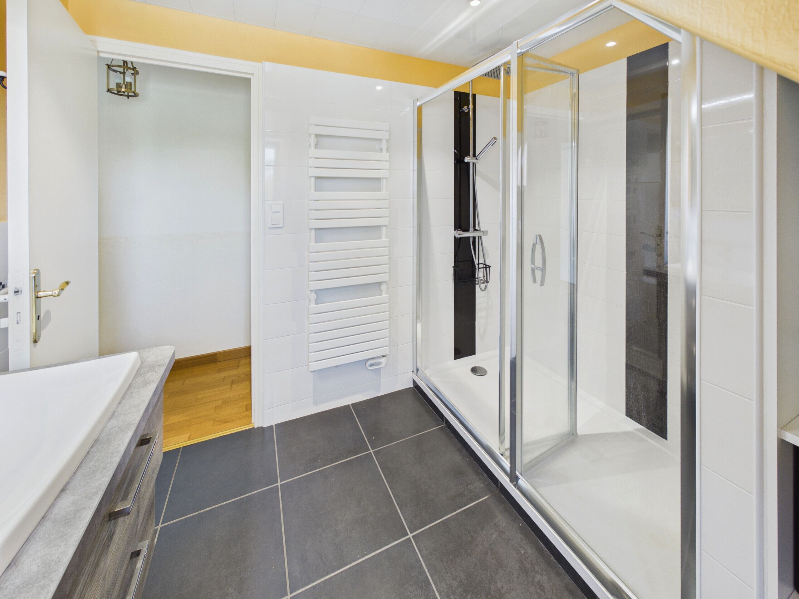 A modern bathroom with a glass-enclosed shower, a white bathtub, and a wooden floor.