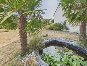 Ein Garten mit Palmen, einem Teich voller Seerosen und einer kleinen Brücke.