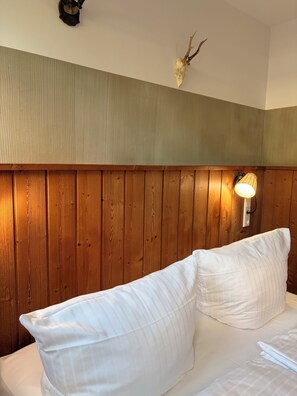 Ein Hotelzimmer mit einem hölzernen Kopfteil, einem aufgehängten Hirschschädel und einer Wandleuchte.