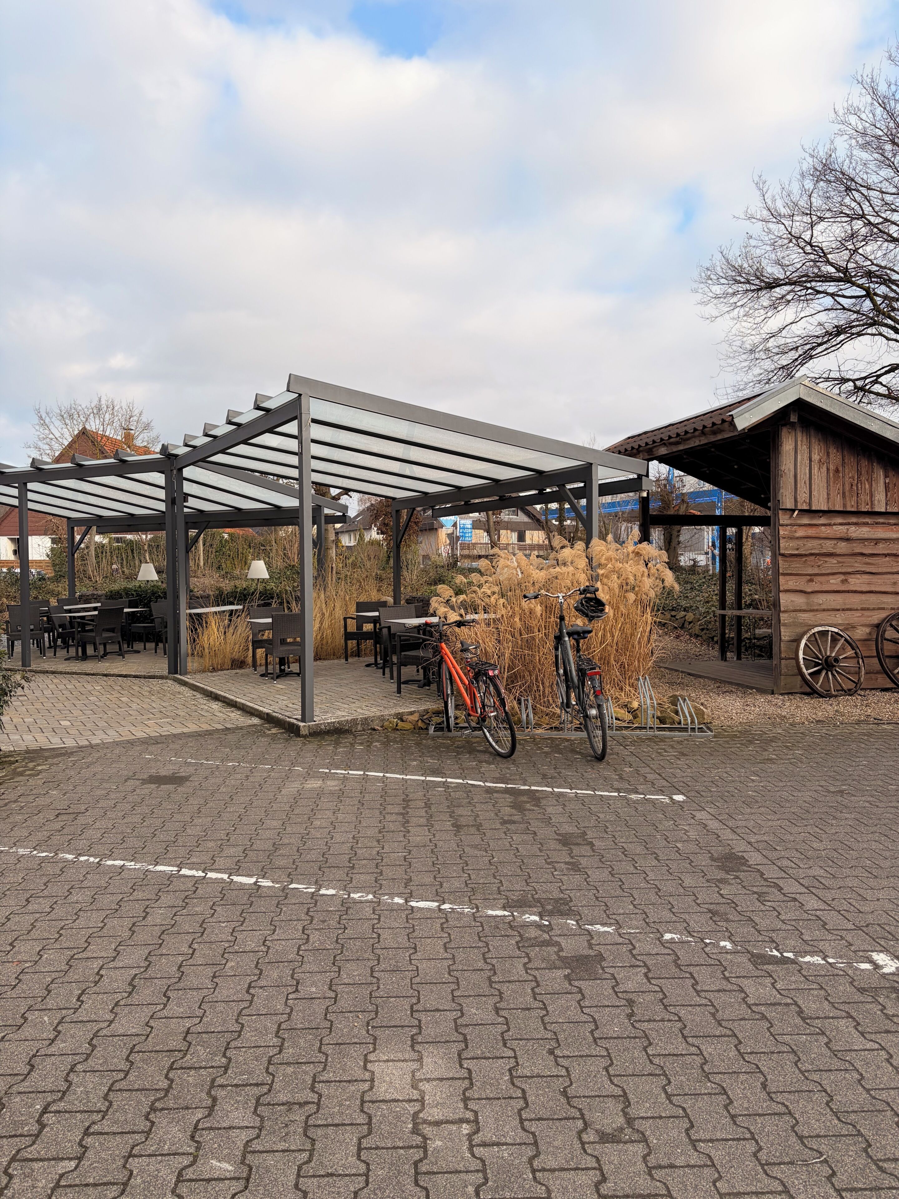 Ein Außenbereich mit Tischen, Stühlen, einem Fahrrad und einer Holzkonstruktion.