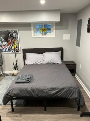 Un dormitorio con cama, mesita de noche, lámpara y un cuadro en la pared.